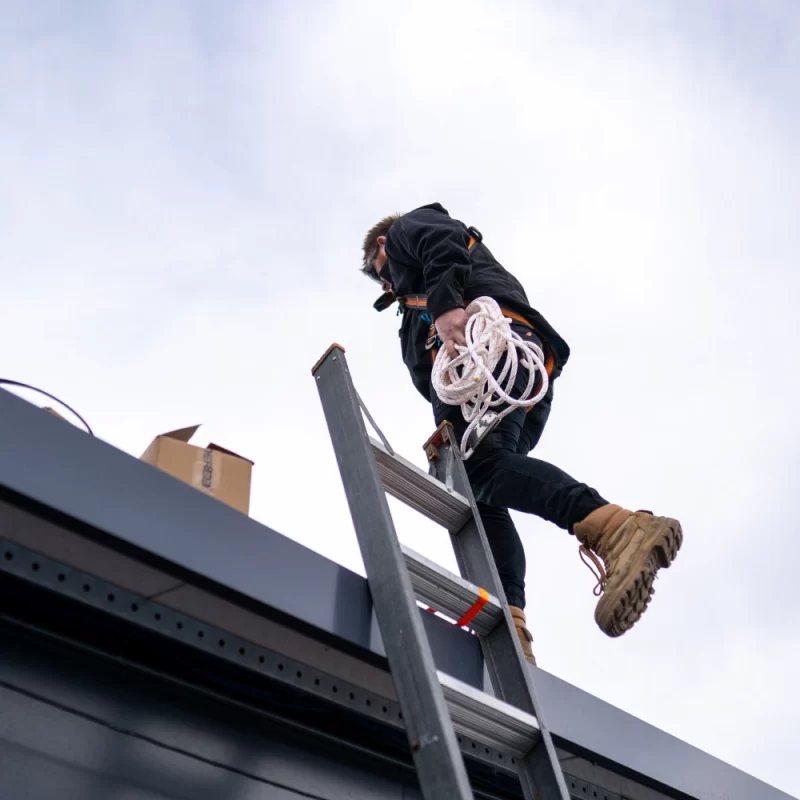 A man on a ladder in hi-vis is undertaking electrical rewiring. Hobart’s HIB Electrical can assist with similar projects.